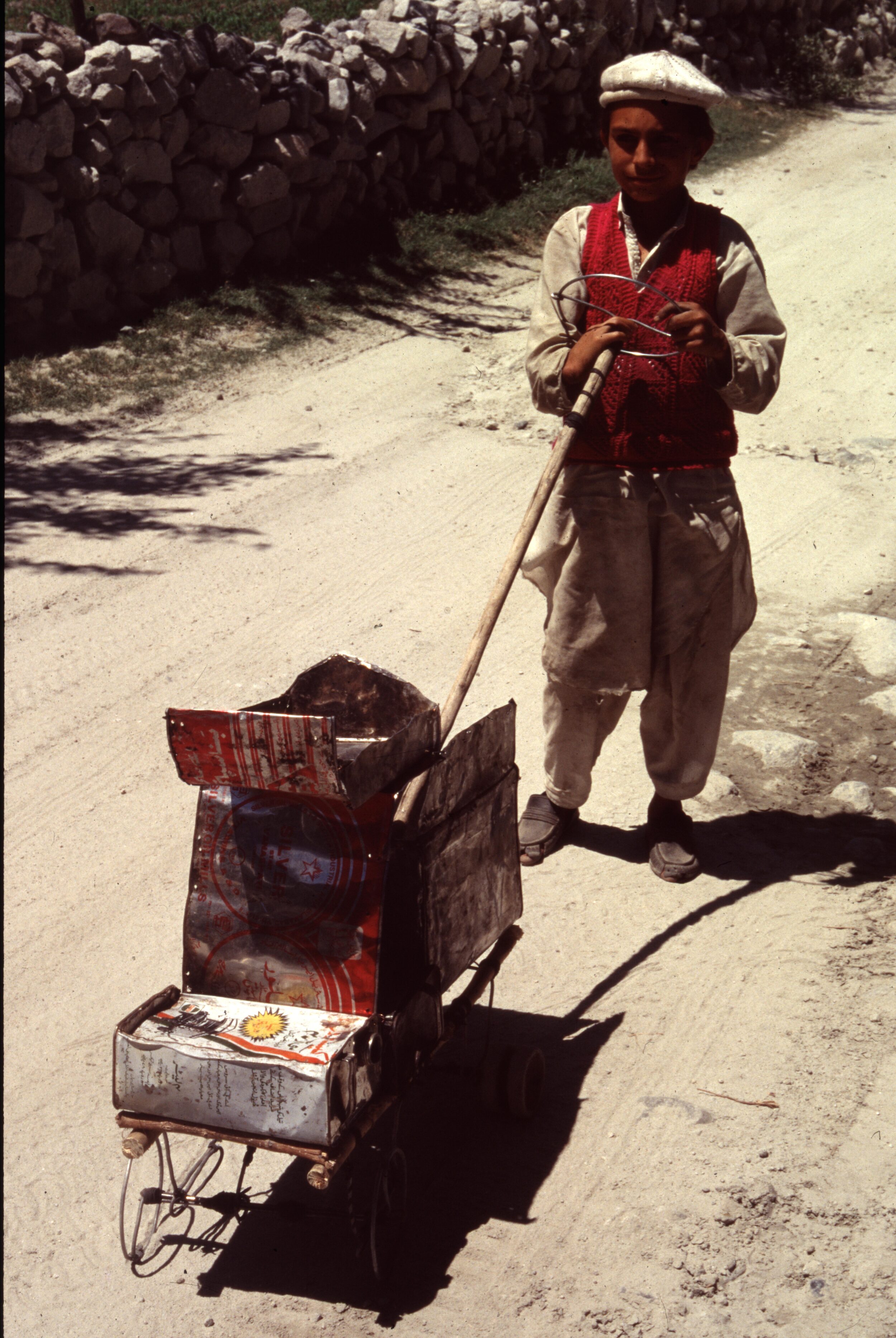 Kind in Pakistan am Karakorum-Highway mit handgemachtem Transportfahrzeug